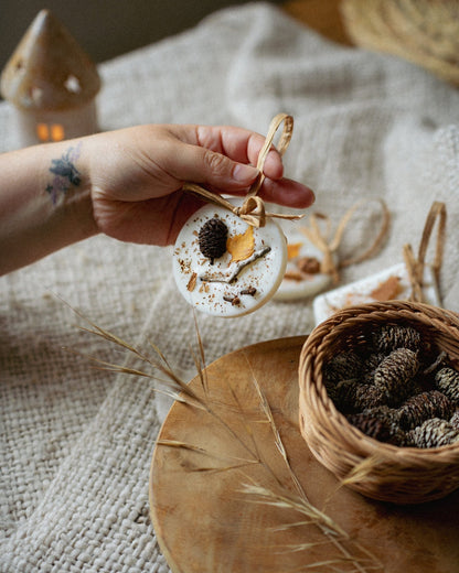 Hand holding a small decorative item with a textured surface, surrounded by natural elements on a textured fabric background.