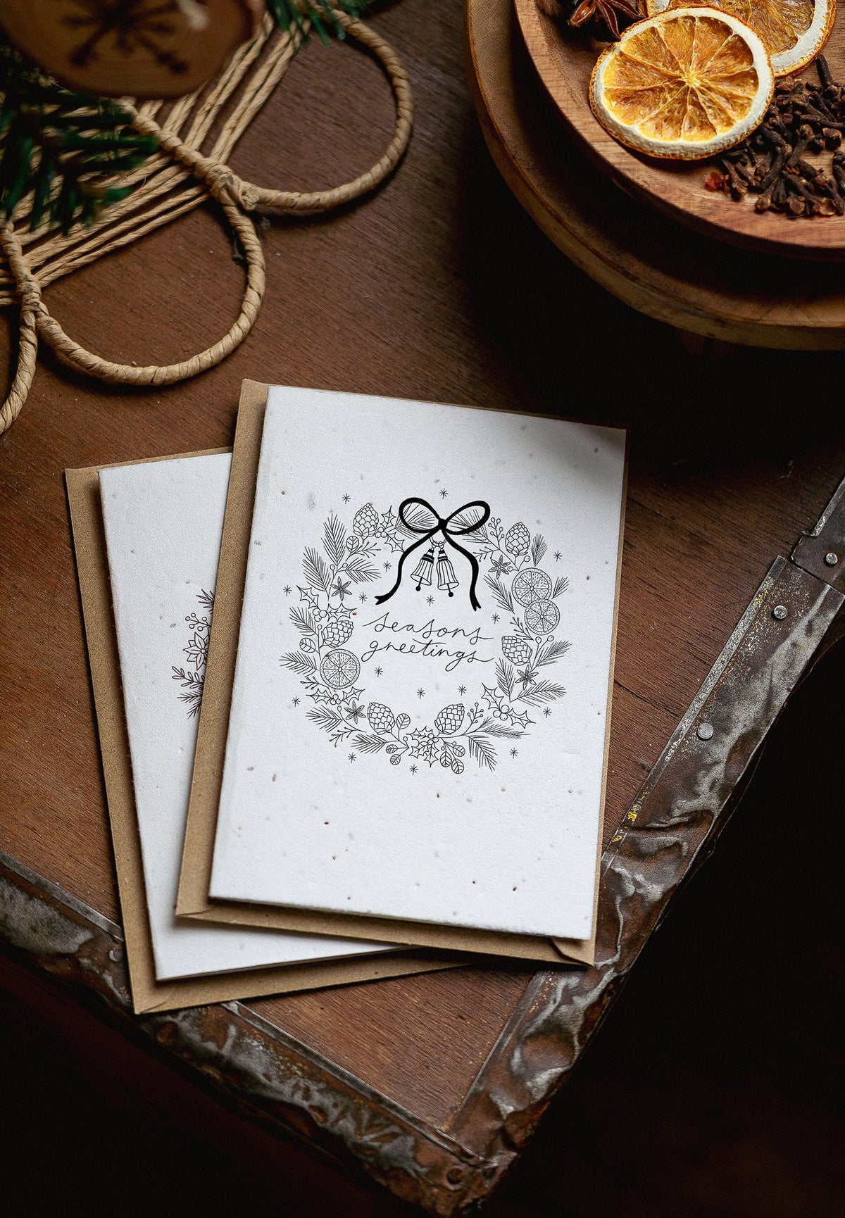 Stack of greeting cards with a decorative design on a wooden surface with dried oranges and pine cones.