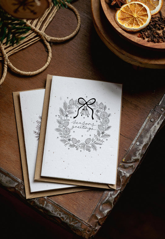 Stack of greeting cards with a decorative design on a wooden surface with dried oranges and pine cones.
